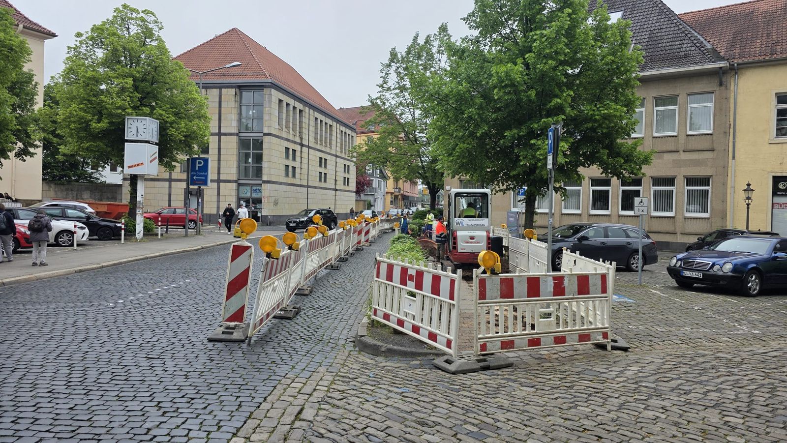 Obra de canalización de fibra con miniexcavadora y vallado de seguridad en una plaza adoquinada de Alemania